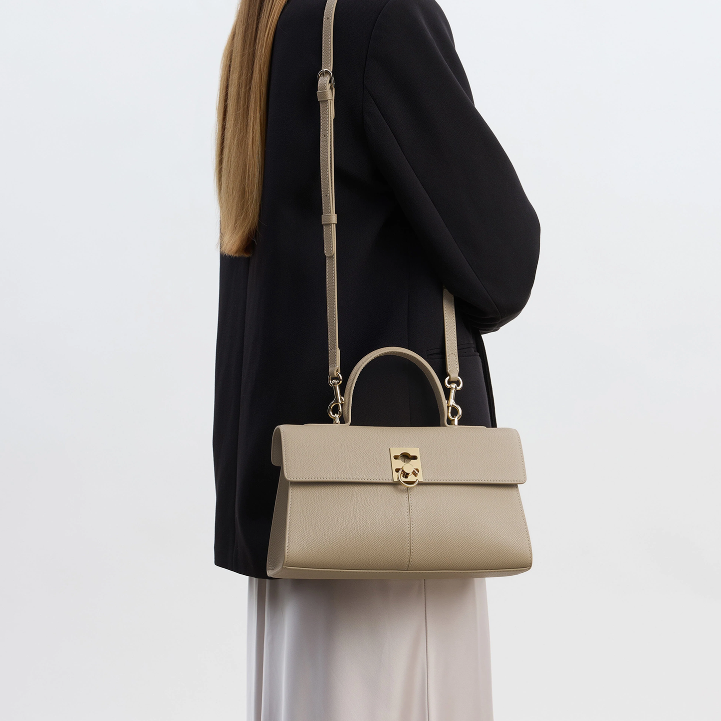 Muted Warm Taupe Fine Grain Elongated Structured Flap Hand Bag With Polished Gold Ring Clasp And Rear Zippered Storage Pocket